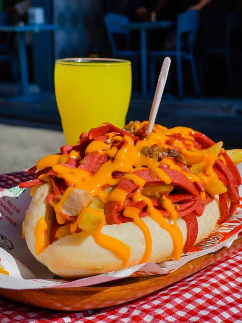 Free A vibrant shot of a cheesy hot dog with various toppings paired with a refreshing drink outdoors. Stock Photo