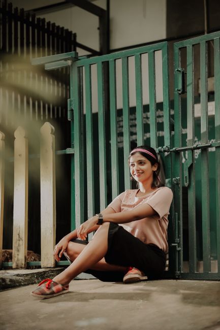 A young woman sitting outdoors, smiling and relaxed, in front of a green gate.