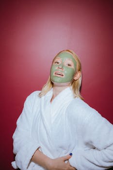 A woman wearing a bathrobe and facial mask poses against a bold red background, embodying self-care and relaxation.