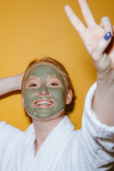Cheerful woman in a face mask and robe giving a peace sign against a vibrant background.