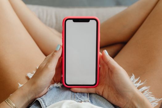 Close-up of a woman holding a smartphone in denim shorts, showcasing the phone display.