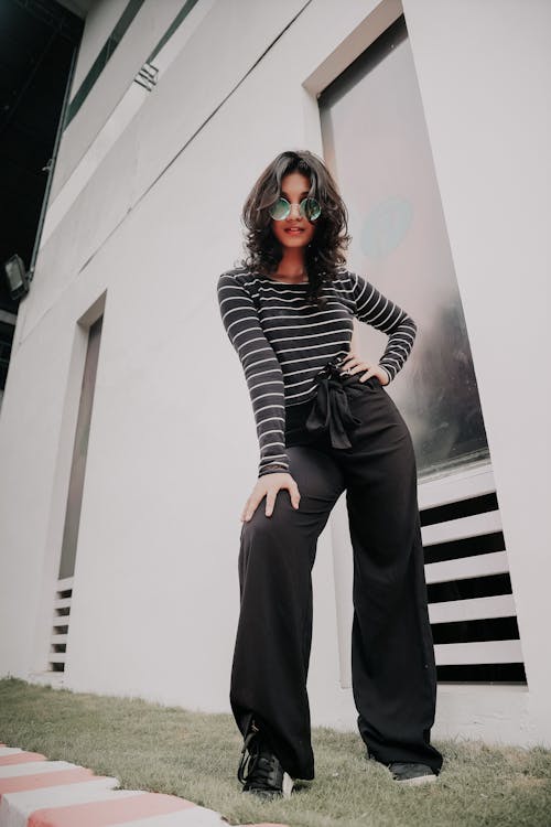 Woman in Black and White Striped Long Sleeve Shirt and Black Pants Standing Beside White Wall