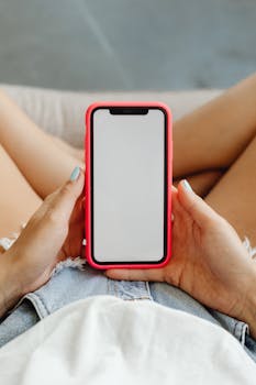 Close-up image of a smartphone with blank screen held by a woman in casual shorts.