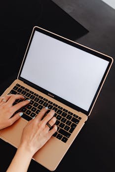 Close-up of hands typing on a MacBook with an empty screen and space for copy.