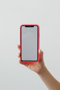 Close-up of a hand holding a smartphone with red case on white background.