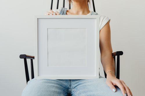 Free A woman sitting indoors holding a blank picture frame on her lap, offering copy space. Stock Photo