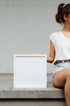 A woman in casual attire holding a blank white picture frame, ideal for mockups.