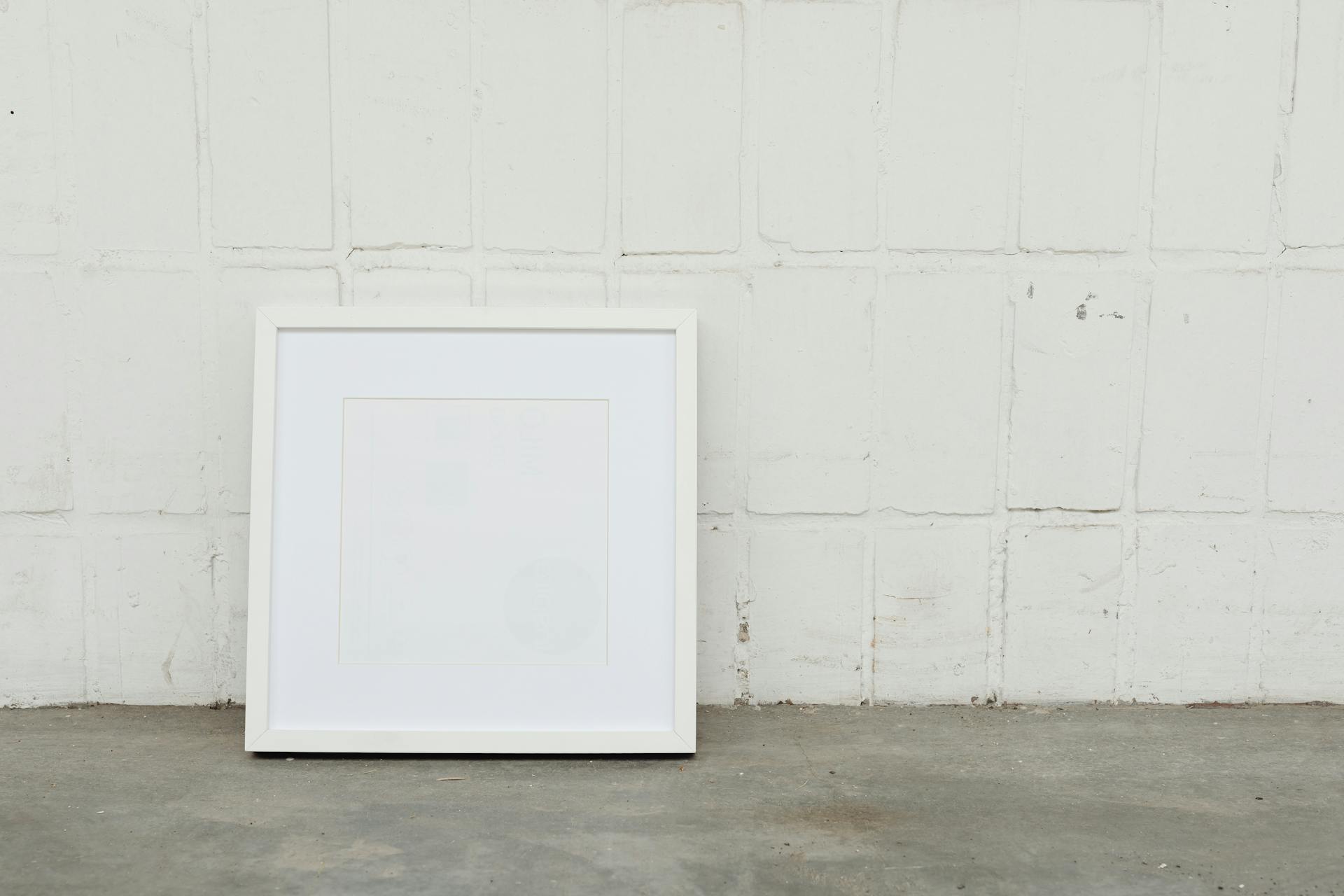 A minimalist white picture frame against a textured concrete wall, offering ample copy space.