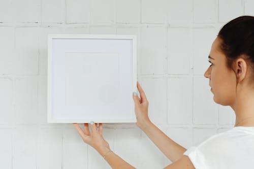 Free A Woman Hanging a Picture Frame on a Wall  Stock Photo