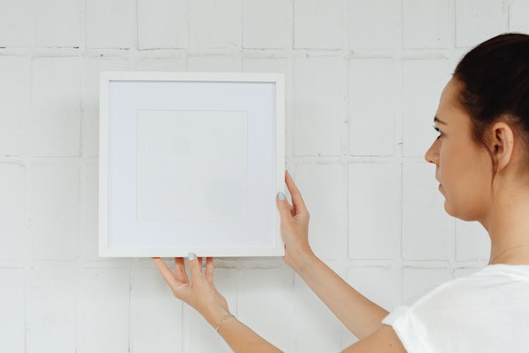 A Woman Hanging A Picture Frame On A Wall 