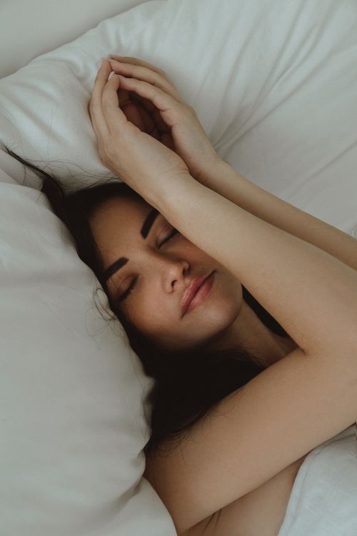 Free A serene image of a woman peacefully sleeping on comfortable white bedding indoors. Stock Photo