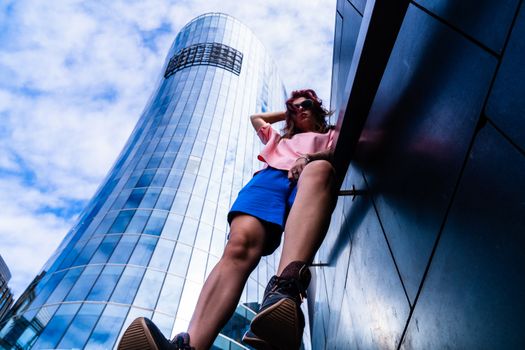 Dynamic low-angle view of a fashionable woman posing near a modern skyscraper in Saint Petersburg.