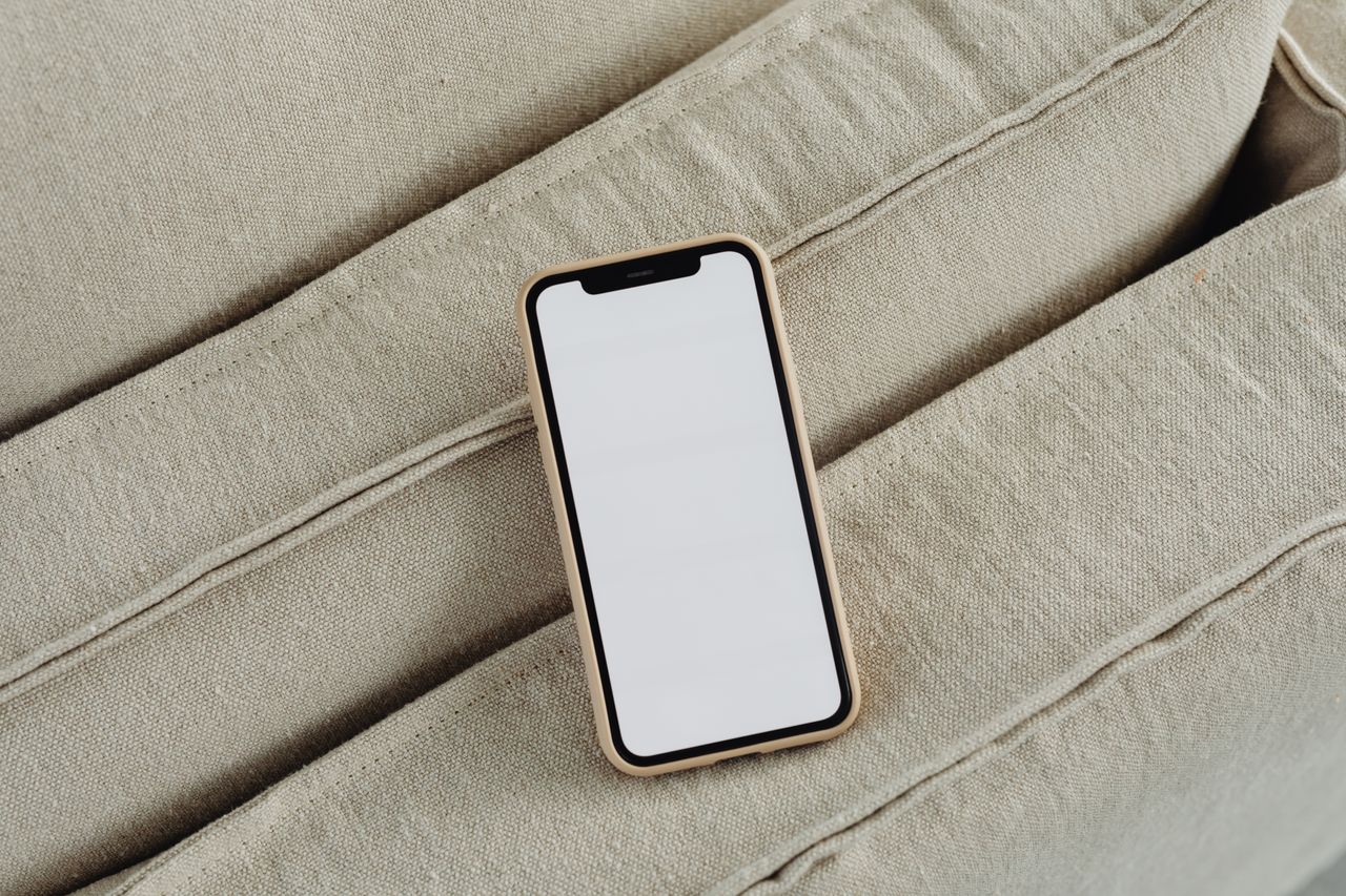 top view of a smartphone on a beige couch featuring a blank white scre