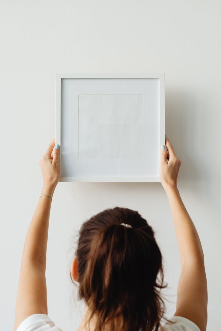 A Woman Hanging An Empty Picture Frame 