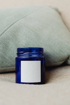 Close-up of blue glass jar with blank label against a textured pillow backdrop.