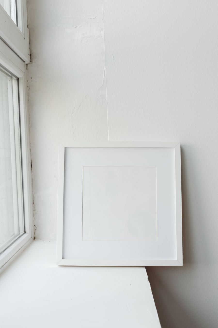 A white frame with a mat resting by a window