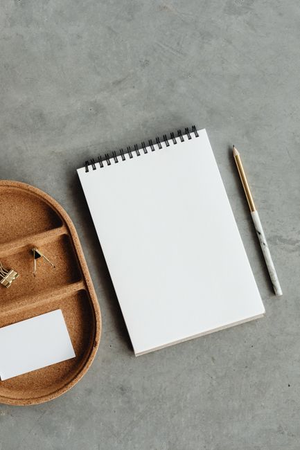 Flat lay of notepad, pencil, and binder clips on a grey surface, ideal for business mockups.