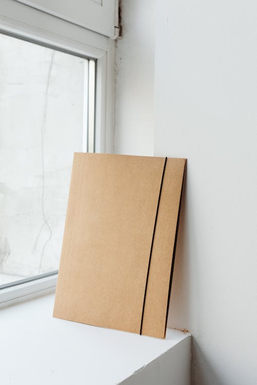 Close-Up Shot of a Brown Cardboard Folder near Glass Window
