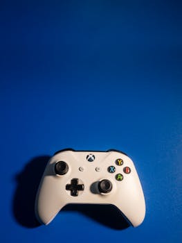 A white Xbox game controller set against a bold blue background, showcasing modern gaming equipment style.