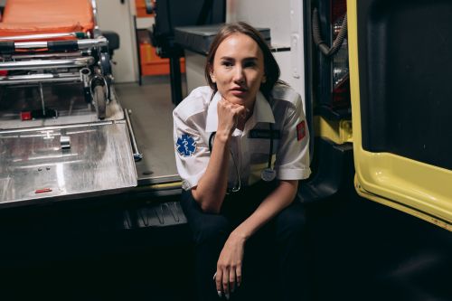Free A female paramedic in uniform sits thoughtfully inside an ambulance, showcasing emergency readiness. Stock Photo
