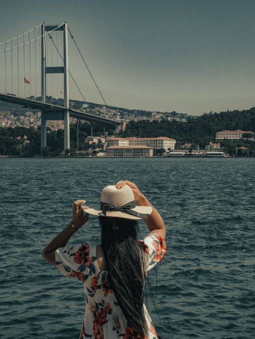Free A woman wearing a straw hat gazes at the Bosphorus Bridge in Istanbul, capturing a serene moment. Stock Photo