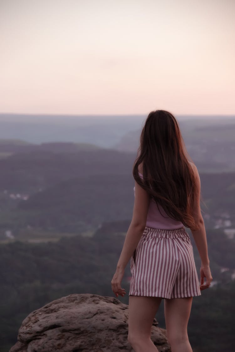 Woman Standing On Top Of Mountain Overlooking Valley