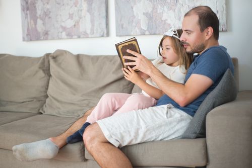 Free A father and daughter share a cozy reading moment on a sofa, bonding over a book. Stock Photo