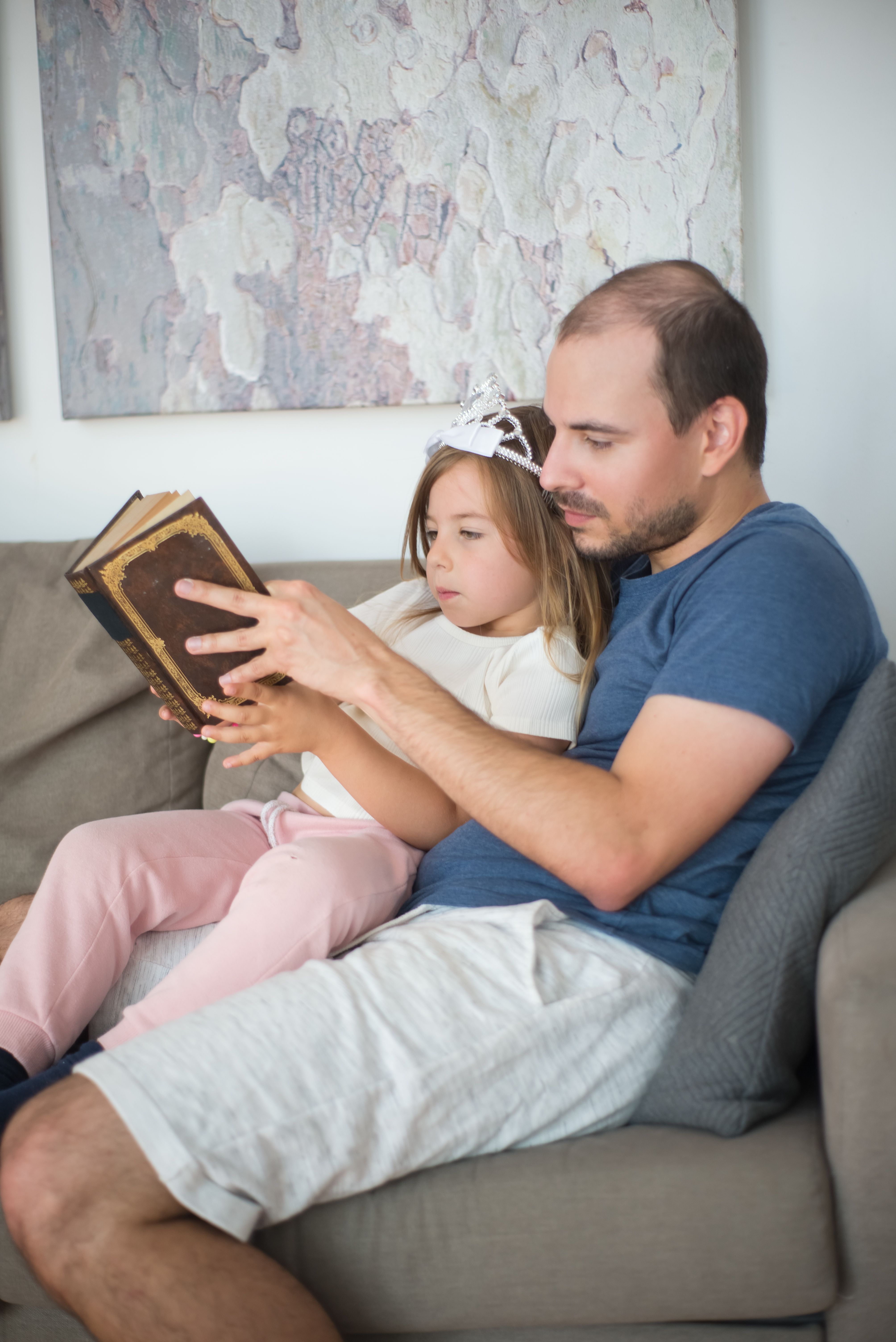 A father and daughter enjoy bonding time reading a book on a cozy couch indoors.