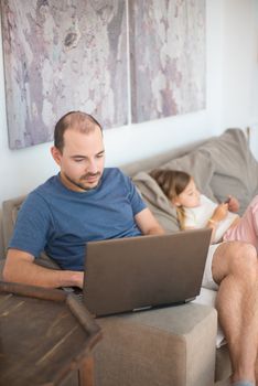 A father and daughter bonding while using a laptop together on the couch at home.