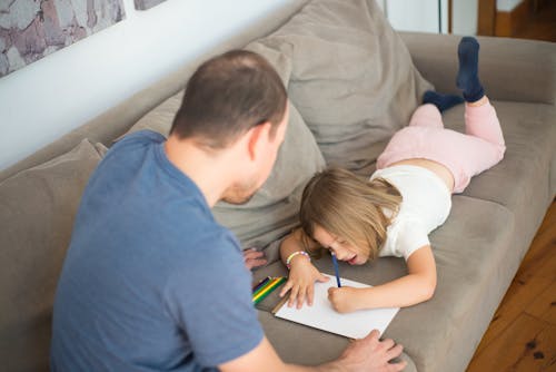 A Girl Drawing while Lying Down on a Couch