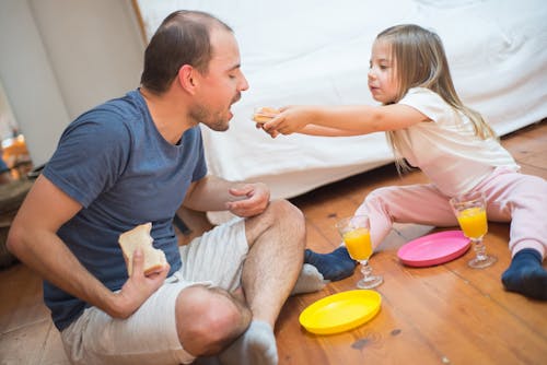 Free Man and Child Sharing Food While Sitting on the Floor Stock Photo