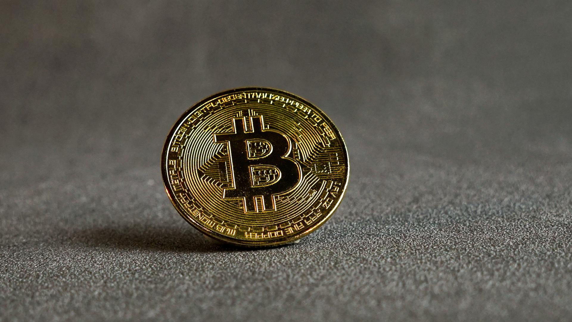 Focused shot of a Bitcoin cryptocurrency coin on a grey backdrop.