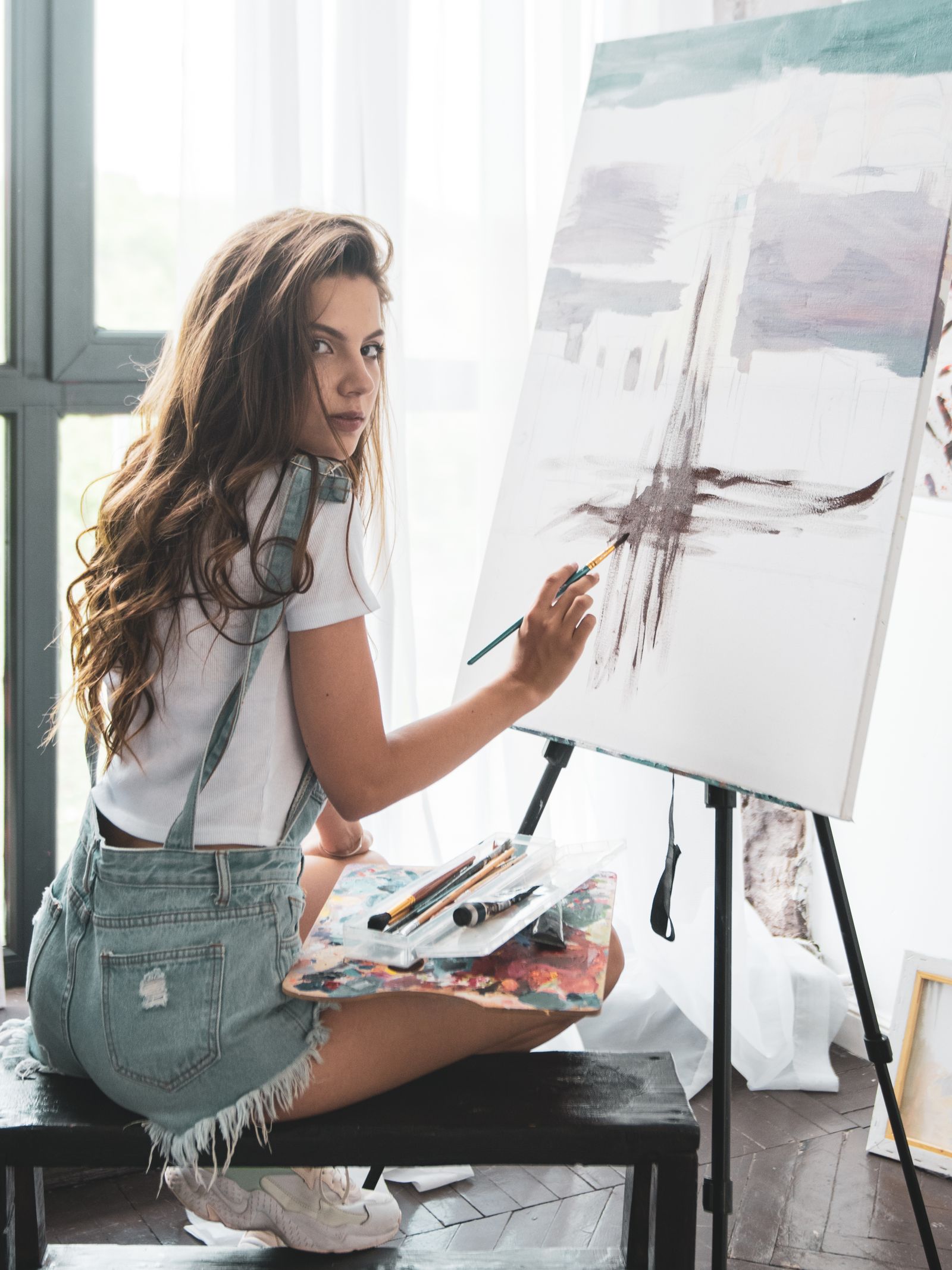 Painter working on a pale canvas beside a bright window