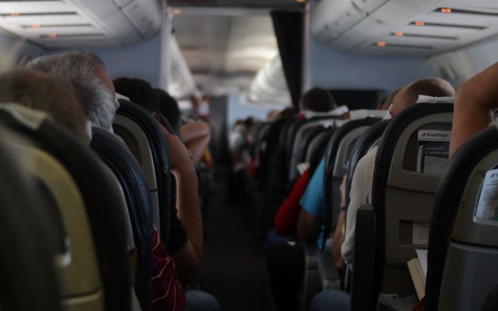 View from the back of an airplane cabin with passengers seated, showcasing travel atmosphere.