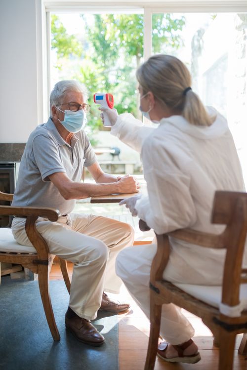 Free A healthcare worker uses a digital thermometer on a senior patient wearing a mask in a clinic setting. Stock Photo