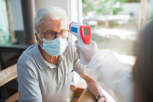 A Person Checking an Elderly Man's Temperature