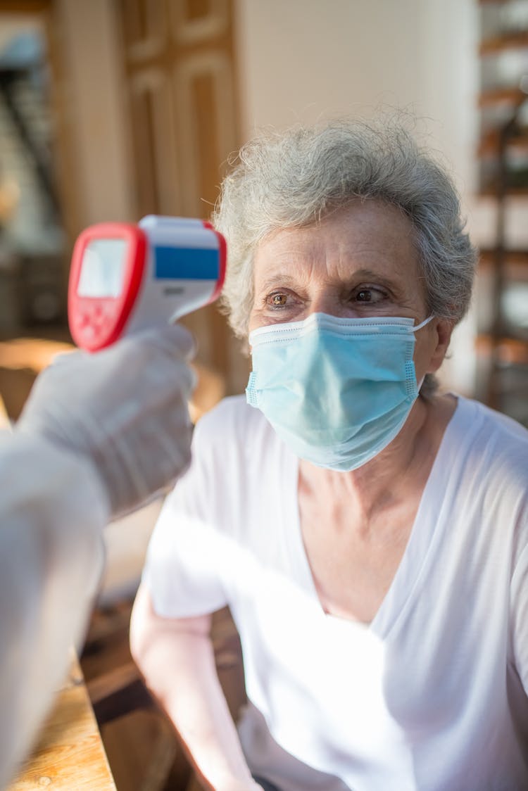 An Elderly Woman Wearing Face Mask Looking At The Thermometer The Hand Is Holding