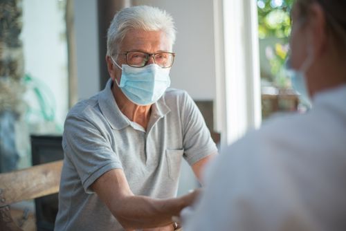 Free Elderly man sitting indoors wearing a mask and eyeglasses during a discussion. Bright and relaxed atmosphere. Stock Photo