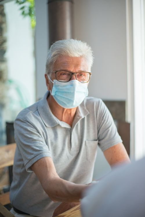 Free Elderly man with face mask sitting indoors during a medical consultation. Stock Photo
