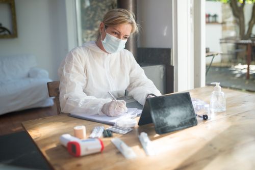 Free Healthcare worker in PPE using a tablet and taking notes indoors, Portugal. Stock Photo