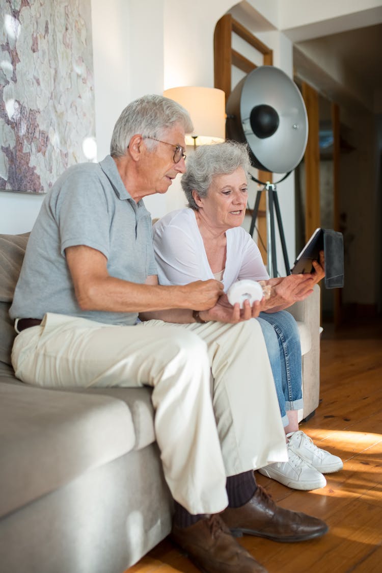 Elderly Couple Sitting On Sofa While Watching On IPad 