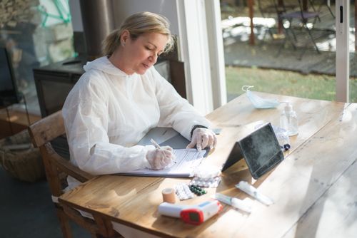 Free A healthcare worker in protective gear documents patient data indoors during daylight. Stock Photo
