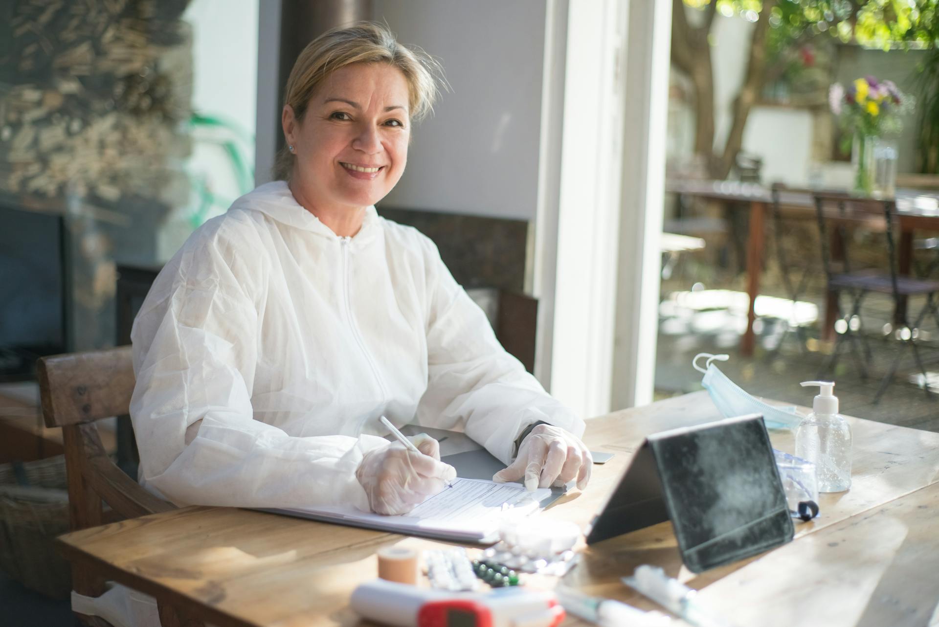 Healthcare worker smiling while writing notes at a desk with medical supplies.