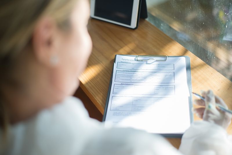 A blank application form on a clipboard between two people, with fields for business name, tax I.D. and trade references.