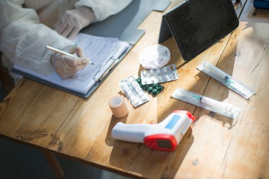 Medical practitioner filling forms with various medical items on desk, showing healthcare preparations.