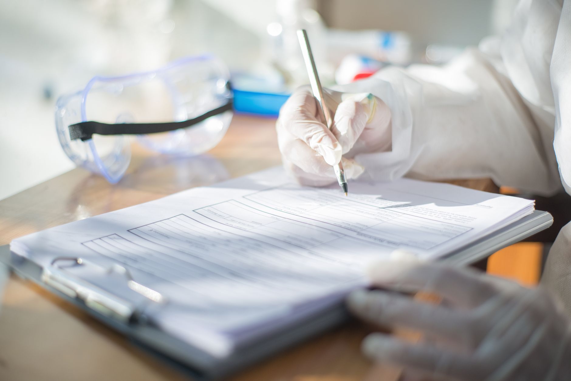 Close-up of a scientist writing on a document with gloved hands in a laboratory setting.