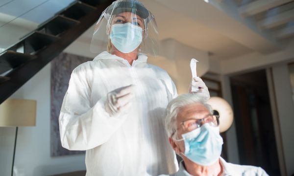 Home Nursing Caregiver — Healthcare professional in protective gear assisting elderly patient in a modern setting.
