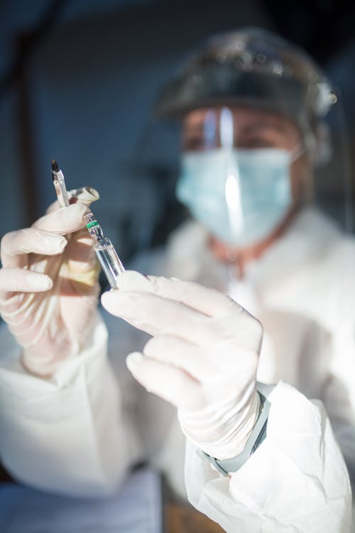 Person in Personal Protective Equipment Holding a Vial