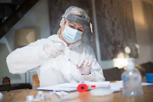 Female healthcare worker in full protective gear prepares a vaccine indoors.