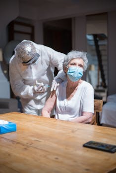 A healthcare worker administers a vaccine to a senior woman wearing a face mask indoors.